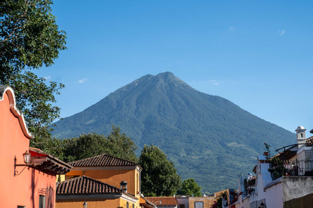 large volcano peak covered in trees towering above ancient city structures in rustic town in south america during a bright summer dayの写真素材