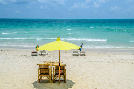 wo chairs a table and a yellow umbrella on the beachの写真素材
