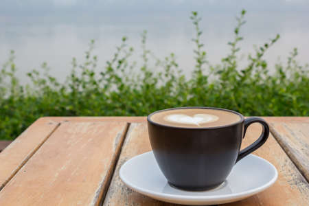 A cup of coffee with heart pattern in a black cup on wooden tableの写真素材