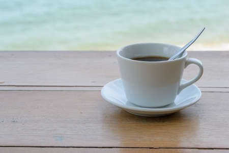 Close up Coffee cup on wood table and view of water sea beachの写真素材