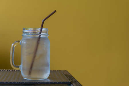 water in glass on table with yellow wall backgroundの写真素材