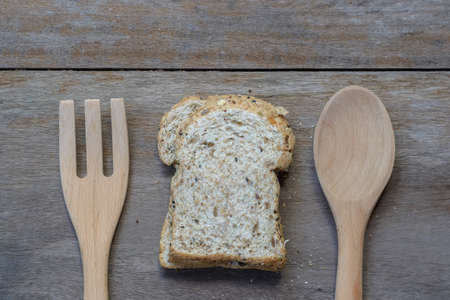 slice of fresh organic whole wheat bread on the old wood background with wooden spoon and fork.の写真素材