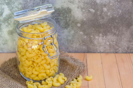 Close-up of Uncooked Macaroni in a glass jar placed on the wooden table with cement wall background , selective focus.の写真素材