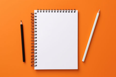 Top view of blank spiral notebook and pencil on orange background with copy spaceの素材