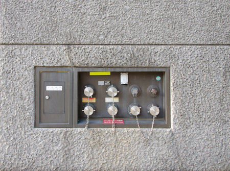 An outdoor sprinkler connection on the side of a building with a brick textured background.