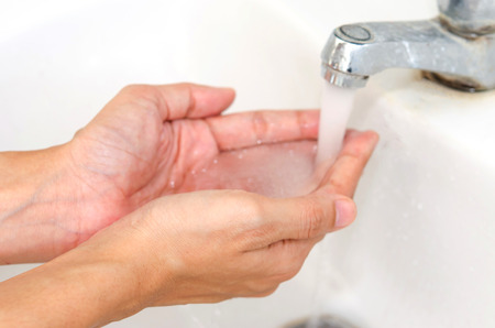 A woman washing her hands with water in a white sink.の写真素材