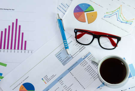 Coffee cup, laptop, notepad and glasses over papers with numbers and charts. View from aboveの写真素材