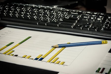 paper work desk and keyboard and pencil report chart on deskの写真素材