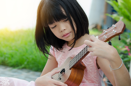 A little girl playing ukulele in the garden.の写真素材
