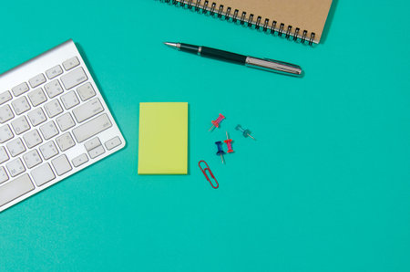 Top view and copy space. Office table desk with note pad, pen, keyboard computer on green...