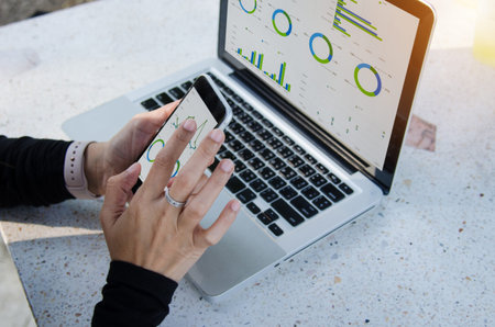 businesswoman working sitting outdoors laptop and smartphone with graphs, diagrams and charts on...