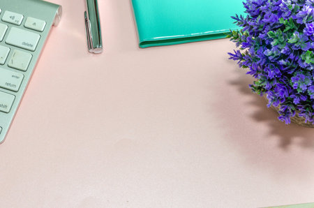 Computer keyboard, pen, green notebook and purple flowers On a pink background. Copy space