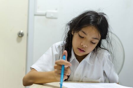 A young asian schoolgirl sitting in a stressful room from homeworkの写真素材