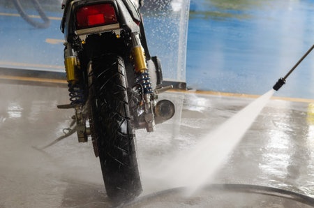 man hand is cleaning with a high-pressure water gun, washing a motorcycle at the car wash shop.