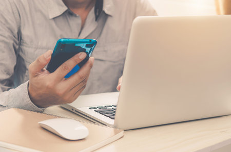 man with a hand holding a smartphone, playing social media, and working at home with a laptop...
