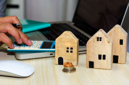 A small wooden house on the desk A man with a pen and a laptop computer and calculator Real estate business concept Property insurance.の写真素材