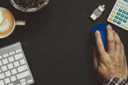 Modern dark office desk table with Office supplies hand holding mouse Calculator , keyboard , coffee and tree  on top view and copy space.Flat lay Business concept desk black table style. Work from home.の写真素材