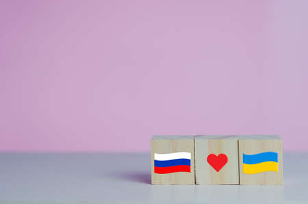 Wooden cubes with russia flag symbol and ukraine flag with red heart icon on background.の写真素材