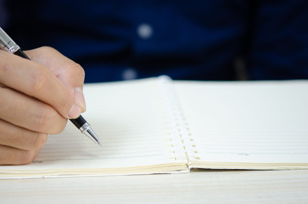 close up holding a pen and writing at the notebook.