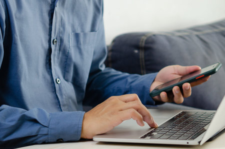 Businessman hand typing keyboard on laptop computer with smart phone. Close up businessman...