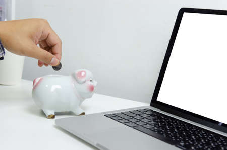 Man hand holding coin at piggy bank finance and computer laptop. business investment saving technology concept.の写真素材