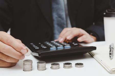 businessman person hand holding coin stack money and calculator on desk.business finance tax growth investment accounting insurance conceptの写真素材