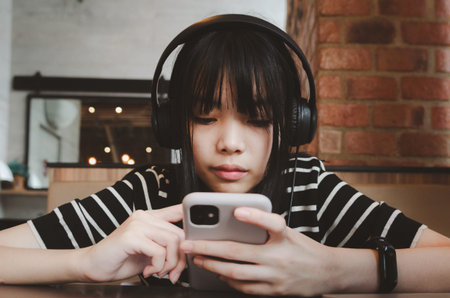 Teenage girl wearing headphones and holding a cell phone smartphone social media relaxing on the...