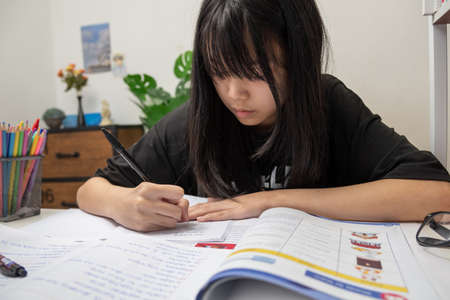 Asian student girl is writing homework and reading book at deskの写真素材
