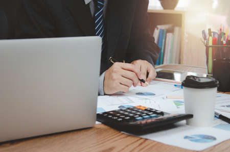 Businessman holding pen document graph accounting finance paper work analysis chart marketing investment and report economy with computer laptop on desk at office.の写真素材
