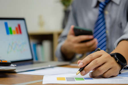 Businessman holding pen document graph accounting finance paper work analysis chart marketing investment and report economy with computer laptop on desk at office.の写真素材