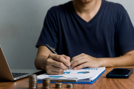 Man holding pen and document graph finance investment report economy tax wealth and analysis profit plan on desk.の写真素材