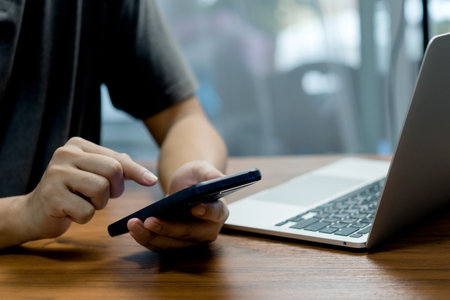 Man hand holding mobile smartphone digital technology network communications at desk.