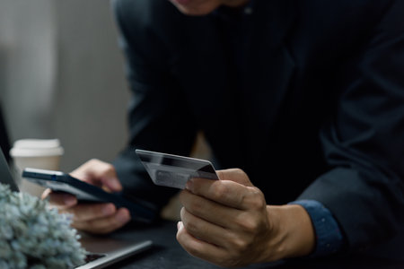 Internet online mobile banking payment digital Technology concept. Man holding credit card shopping e commerce use smart phone and laptop computer.の写真素材