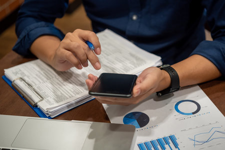 Report charts and graphs marketing financial business analysis and data insights. Hand man holding mobile smartphone on desk.の写真素材