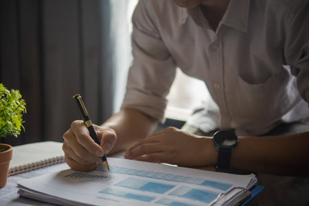 Business man holding pen with analysis financial graph and report marketing statistic chart on desk.の写真素材