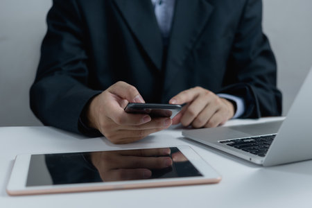 Businessperson using mobile phone and laptop computer tablet job search, communication social networking, internet online on desk.の写真素材