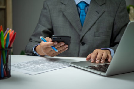 man using smartphone mobile application and document information with laptop on desk.