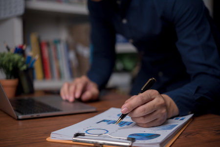 Businessman is using a laptop and pointing to a marketing graph working on analyzing financial...