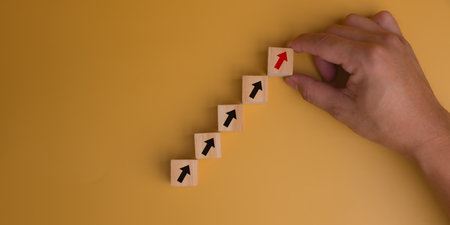 Hand holding wood cube icon arrow up growth performance success development management on yellow background.の写真素材