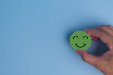 customer service evaluation and satisfaction survey concept. hand holding emotion happy smile face icon on wooden cube on blue background. copy spaceの写真素材