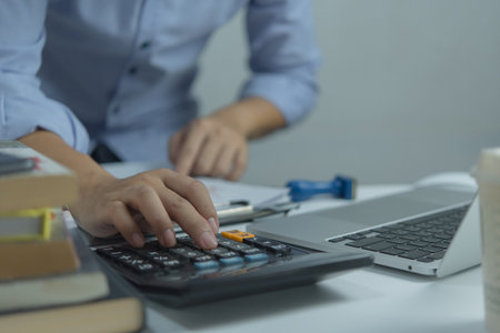 Businessman using calculator and accounting documents at desk with laptop computer.の写真素材