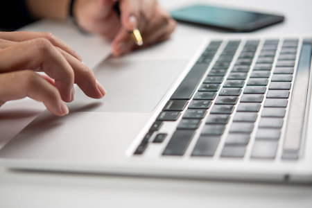 Close-up of hands typing on a laptop keyboard with pen in hand, suggesting business communication