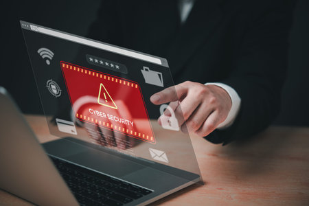 A person is pointing at a computer screen that has a red warning sign that says Cyber Security. The...