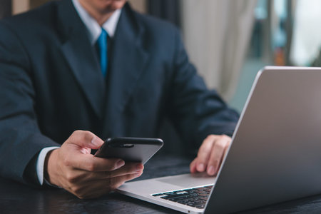 Businessman using phone and laptop simultaneously. Concept of multitasking, modern work environment,...