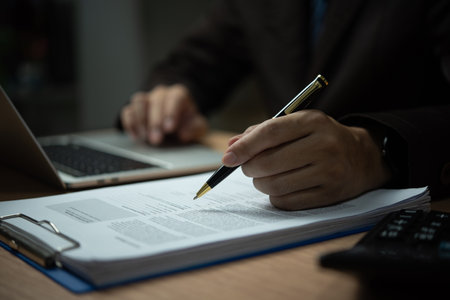 A man is writing on a piece of paper with a pen. He is wearing a suit and tieの写真素材