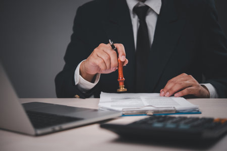 businessman in a suit stamping documents at a desk. Hand holding stamp, giving approval. Professional, authoritative action. Suitable for business, finance, legal,の写真素材