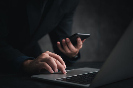 Person using a smartphone while typing on a laptop. Represents modern communication online internet