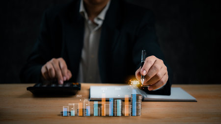 Businessman analyzing growth projections with coins and bar chart up to 2025. Financial strategy, market success, future planning.の写真素材