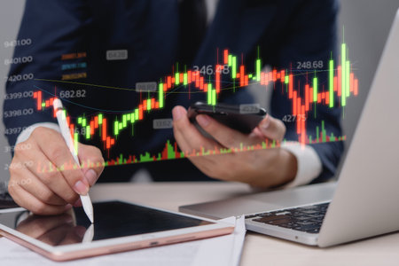 Businessman holding a digital tablet and smartphone, analyzing stock market data with a financial...