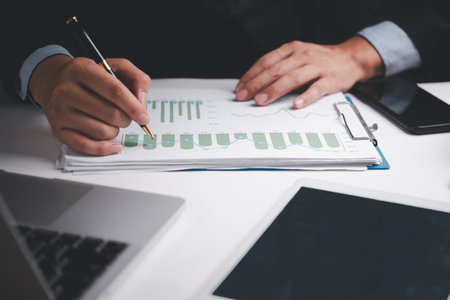 businessman analyzing financial reports and graphs with a pen at his desk, focusing on growth data.の写真素材